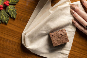 Christmas brownie on cloth with holly decoration and hand reaching in.