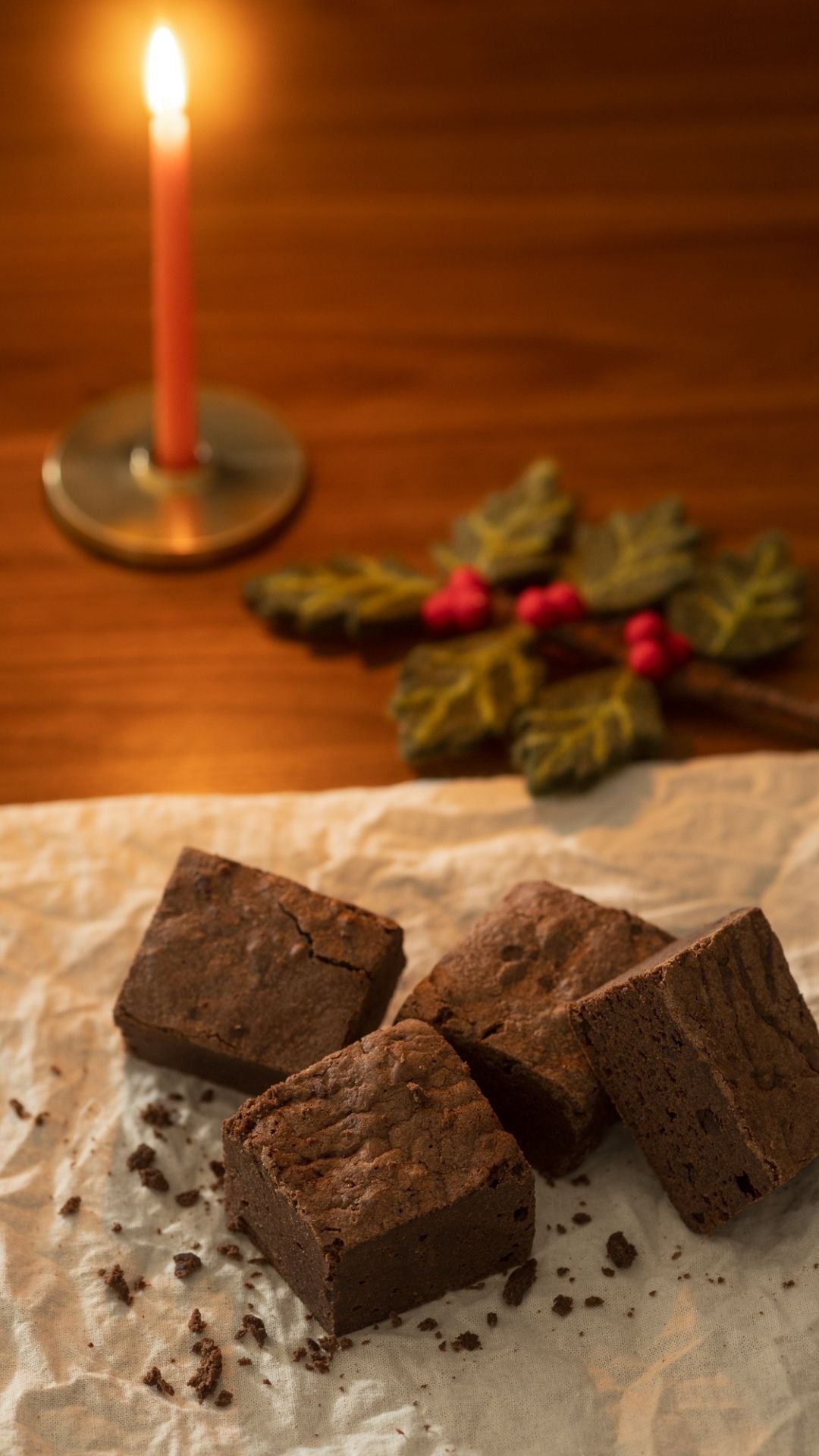Candlelit scene with Christmas brownies on crinkled parchment.