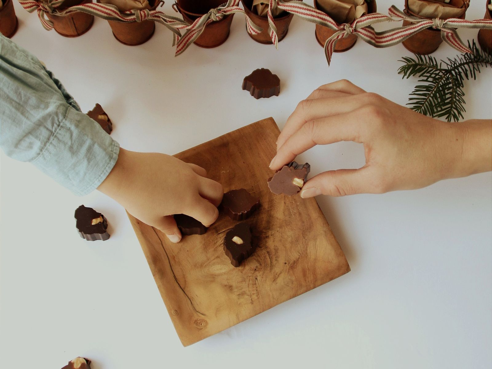 “Hands reaching for handcrafted Bean and Goose chocolate islands during the Advent countdown.”
