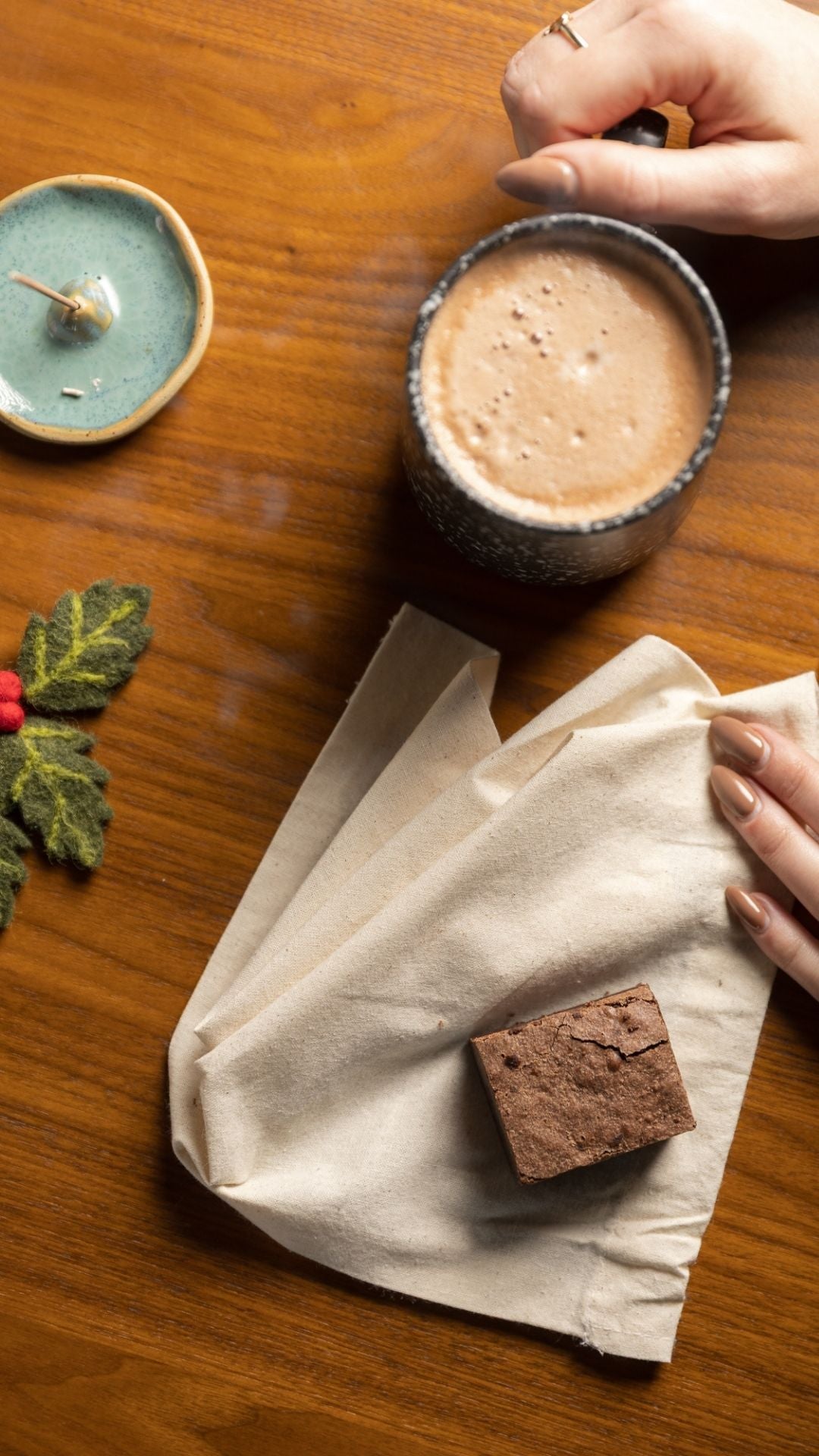 Cup of hot chocolate and brownie on a wooden table with festive holly