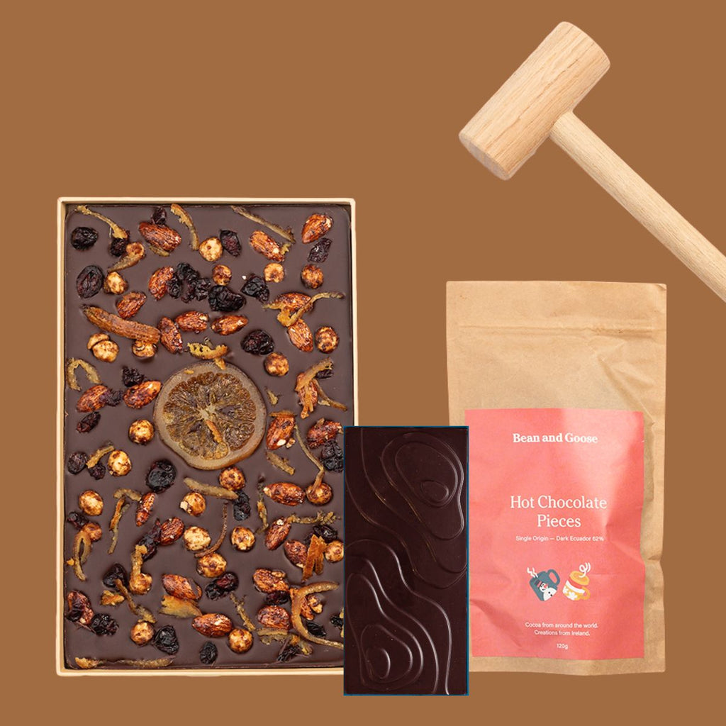 Sharing Slab in a box with an oak hammer, a bar of dark chocolate, and a package labeled 'Bean and Hot Chocolate' on a brown background.